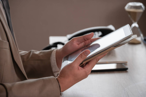 Ofis masasında otururken dijital tabletle çalışan kahverengi takım elbiseli bir işadamı. İş uygulaması ve dijital teknoloji kavramı - Fotoğraf, Görsel
