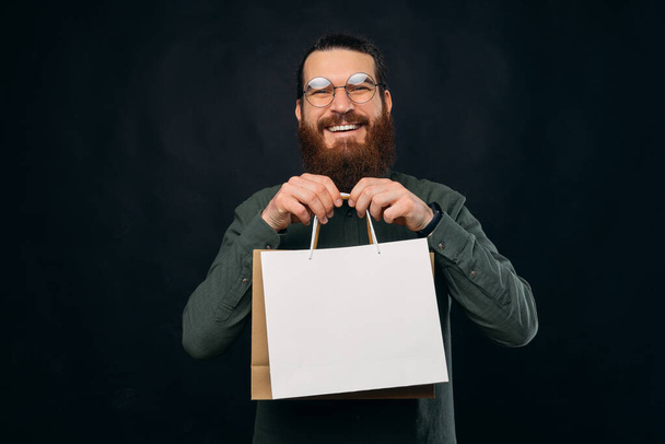 Cheerful bearded man is holding shopping paper bags with copy space on them. - Foto, Imagem