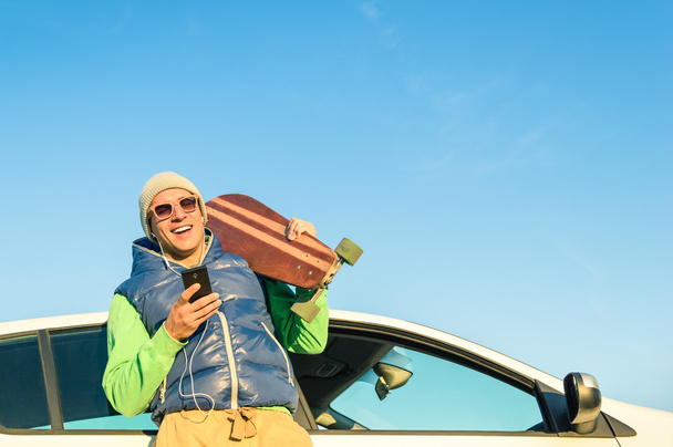 Hipster młody człowiek z smartphone słuchania muzyki obok jego samochód - koncepcji nowoczesnych technologii, zmieszane z rocznika podróż życia - jesień zima młodzieży mody alternatywnej w słoneczny dzień wycieczka - Zdjęcie, obraz