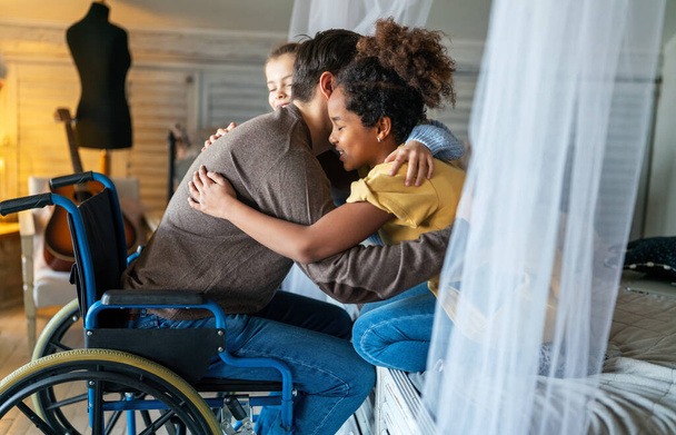 Portrait of happy loving father with disability in wheelchair hugging with multiethnic children. Family, love concept - Photo, image