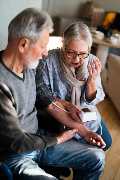 Senior couple at home measuring blood pressure together. Home monitoring people healthcare concept - Foto, Bild