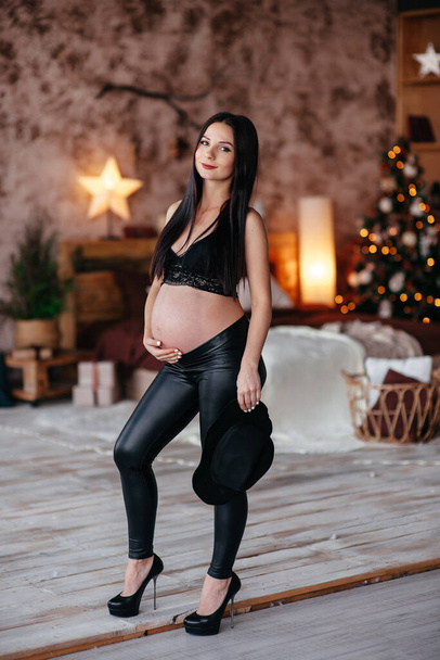 Pregnant woman in black dress sitting on the chair in the studio with white background. Pregnant woman touching belly - Φωτογραφία, εικόνα