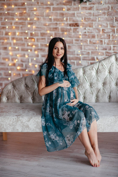 Pregnant bride brunet is preparing to become a mother and wife. Long turquoise dress on a girl's body. Curly hair and a beautiful smile on the woman's face. Two months before birth - Fotografie, Obrázek