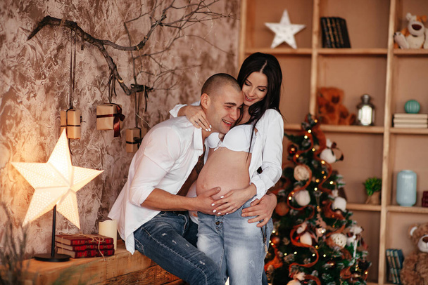Pregnant couple looking ultrasound photo baby in belly. Mom and Dad feeling happy while take care child lying on sofa in living room. - Zdjęcie, obraz