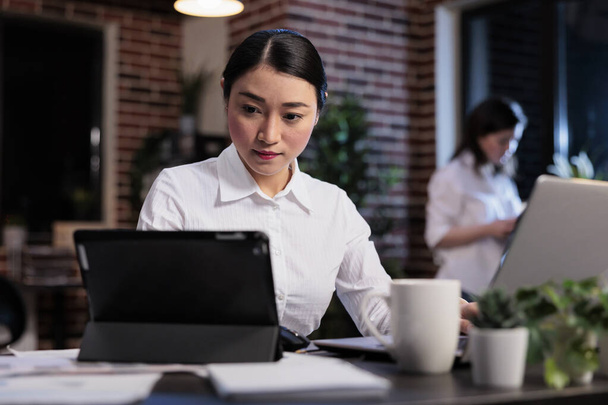 Mujer de negocios asiática con tableta moderna revisando la documentación contable en el espacio de trabajo de la oficina. - Foto, imagen