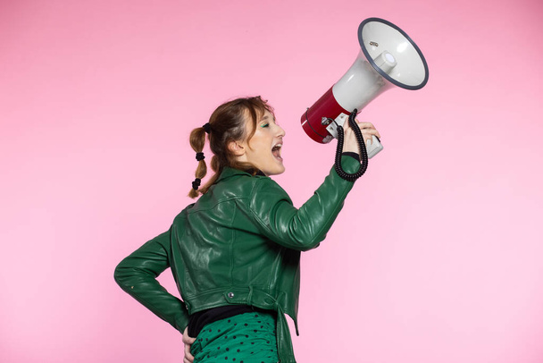 Funny young female shouting through megaphone. Young woman using loudspeaker on colored backgrounds - Photo, Image