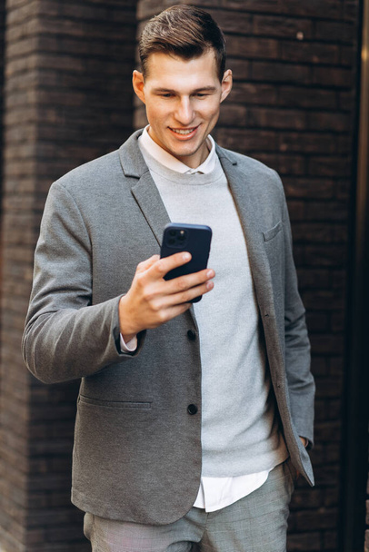 Bonito homem sorrindo moderno andando pela rua e falando ao telefone - Foto, Imagem