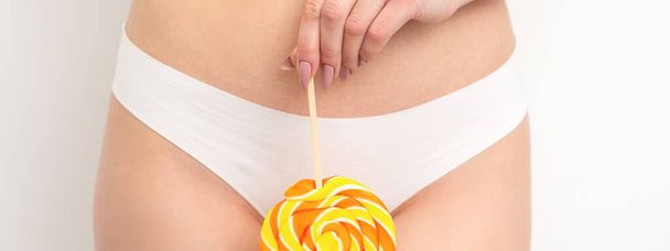 Hand of a woman wearing white panties holding lollipop on a stick covering the intimate area, the concept of intimate depilation, problems of intimate hygiene - Photo, Image