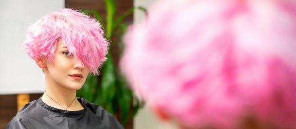 Красива молода біла жінка з новою рожевою короткою зачіскою у дзеркальному відображенні дивиться на камеру в перукарні
 - Фото, зображення