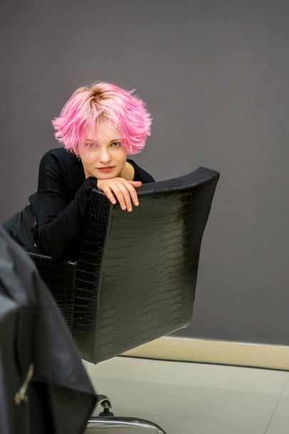 新しい短いピンクのヘアスタイルを持つ美しい若い白人女性の肖像ヘアドレッサーサロンで椅子に座って - 写真・画像