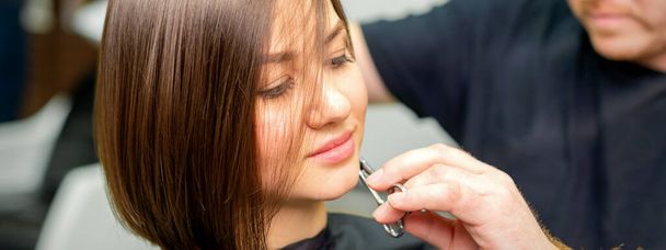 The hairdresser cuts the hair of a brunette woman. Hairstylist is cutting the hair of female client in a professional hair salon, close up - Photo, Image