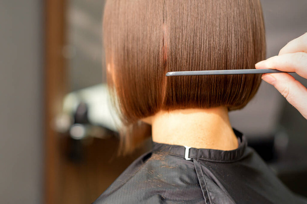 Bir kuaför kuaför kuaför salonundaki esmer kadının kısa saçlarını tarıyor. - Fotoğraf, Görsel