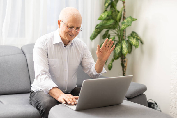Online leraar met koptelefoon aan de balie. Een oudere man werkt aan een laptop.. - Foto, afbeelding