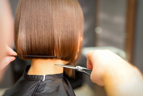 Стрижка коротких волос молодой белой женщины руками парикмахера в парикмахерской, вид сзади, крупным планом - Фото, изображение