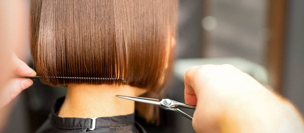 Kurzhaarschnitt einer jungen weißen Frau durch die Hände eines Friseurs in einem Friseursalon, Rückansicht, Nahaufnahme - Foto, Bild