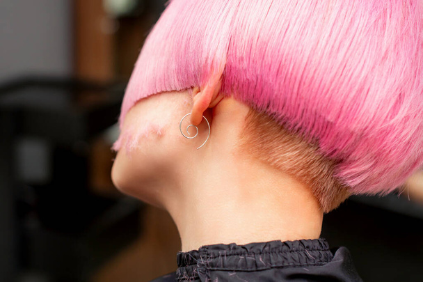 Styling and cutting dyed pink hair of young model back view in a hairdressing salon. Pink short hairstyle - Фото, изображение