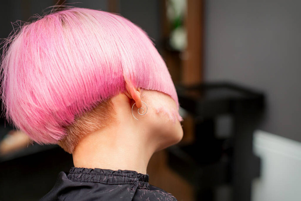Bir kuaförde genç bir modelin pembeye boyanmış saçlarını şekillendirip kesiyor. Pembe kısa saç stili - Fotoğraf, Görsel