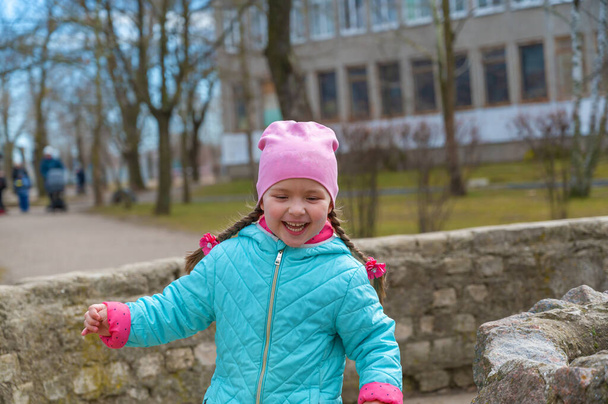 Una chica traviesa y feliz corriendo por el parque de la ciudad. Un niño de cinco años con el pelo largo trenzado en coletas. - Foto, imagen