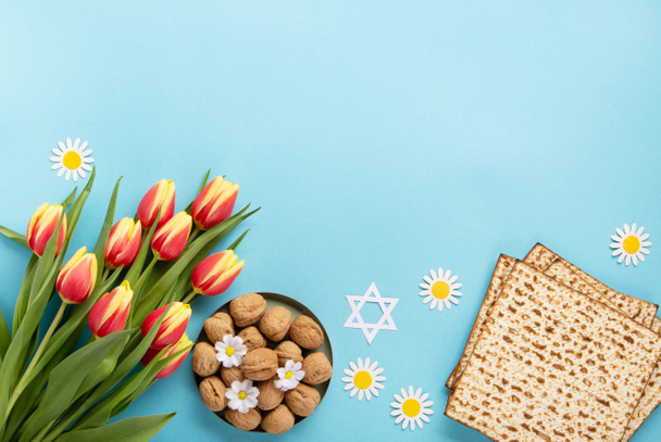 Jewish holiday Passover greeting card concept with matzah, nuts, tulip and daisy flowers on blue table. Seder Pesach spring holiday background, top view, copy space. - Foto, Imagem