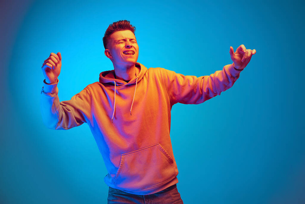 Studio shot of young emotional man, student dancing isolated over blue studio background. Action, sport, fashion - Zdjęcie, obraz