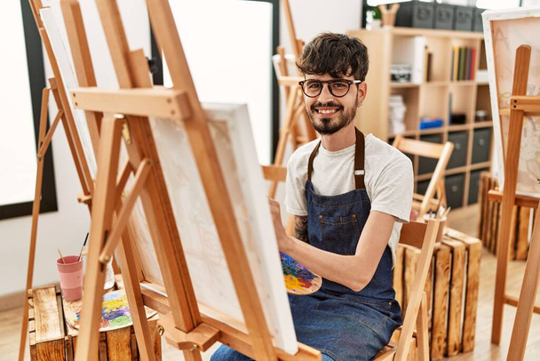 Νεαρός Ισπανός καλλιτέχνης χαμογελά χαρούμενος σχέδιο στο στούντιο τέχνης. - Φωτογραφία, εικόνα