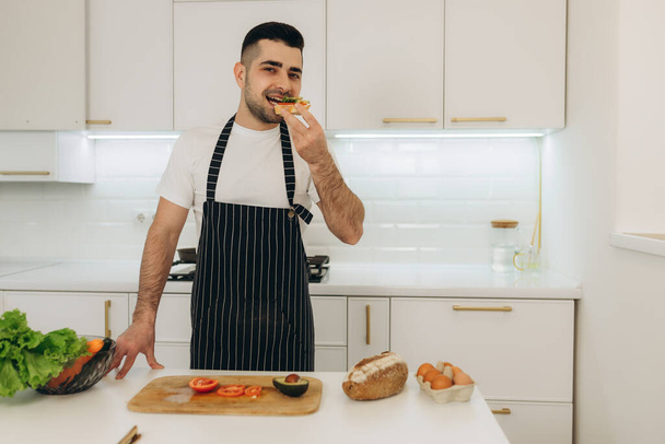 Mutfakta yakışıklı bir adamın portresi. Elinde pişmiş avokado tostu var. Organik kahvaltı. - Fotoğraf, Görsel