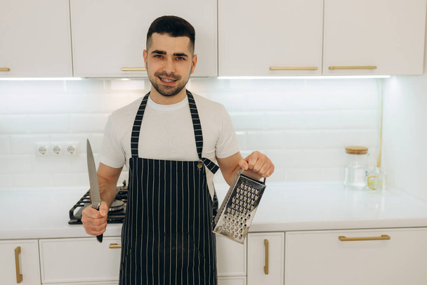 Retrato de un hombre chef sosteniendo un cuchillo de cocina y rallador - Foto, Imagen