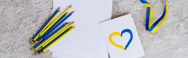 vista superior de lápices azules y amarillos, cinta y tarjeta con el signo del corazón en gris alfombra esponjosa, pancarta - Foto, Imagen