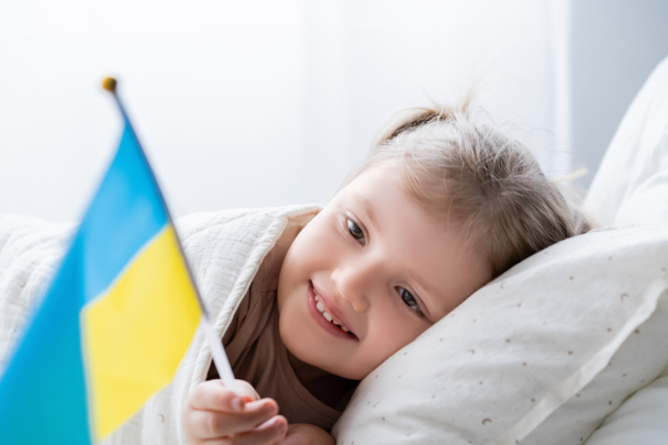 patriottisch meisje liggend in bed thuis en met kleine Oekraïense vlag - Foto, afbeelding