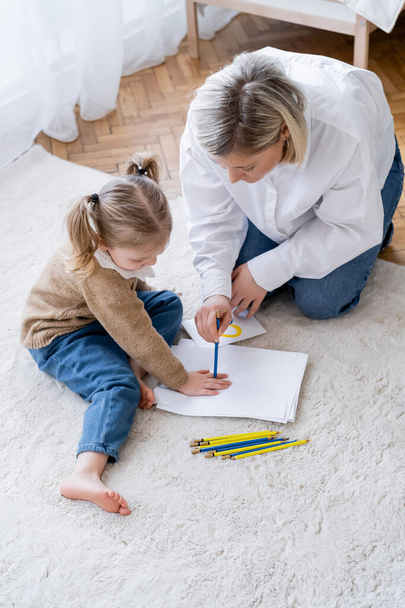 high angle view of blonde woman and girl with ponytails drawing on floor at home - Fotografie, Obrázek