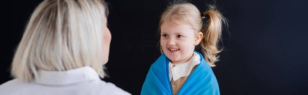 little girl with ponytail smiling near blurred mother isolated on black, banner - Photo, image