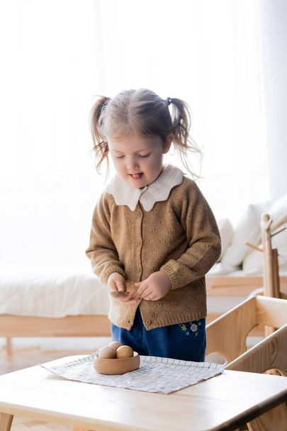menina saindo língua enquanto explorações colher perto tigela com bolas de madeira - Foto, Imagem