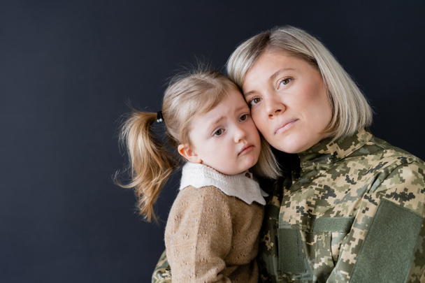 vrouw in camouflage kijken naar camera in de buurt boos dochter geïsoleerd op zwart - Foto, afbeelding