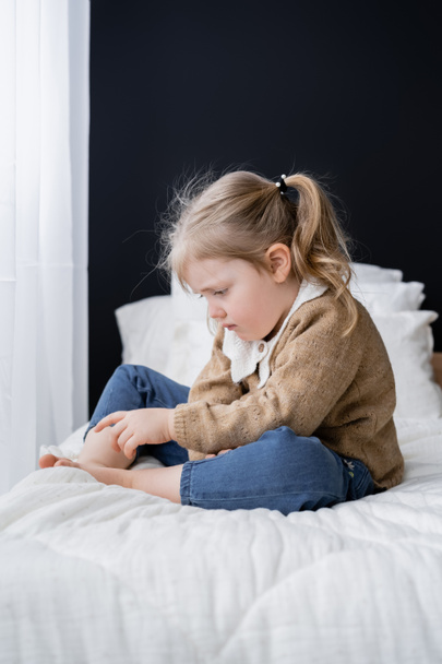 upset barefoot child sitting on bed at home - Foto, afbeelding