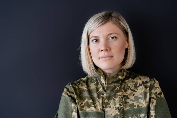 Blondine in Militäruniform blickt isoliert auf schwarze Kamera - Foto, Bild