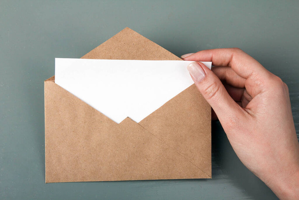 vrouw neemt brief van envelop op grijze houten achtergrond - Foto, afbeelding