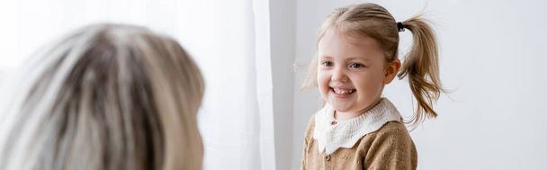 cheerful girl looking at mom on blurred foreground at home, banner - Valokuva, kuva