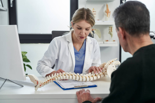 Caucasien femme médecin parler avec patient au sujet de sa colonne vertébrale  - Photo, image