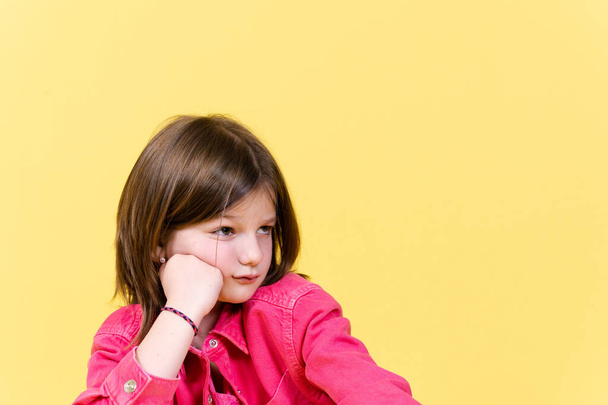 Trauriges kleines Mädchen schaut auf gelben Kopierraum - Foto, Bild