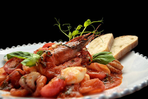 Морепродукты с креветками, мидиями, кальмарами и гребешками на белой тарелке, на темном фоне - Фото, изображение
