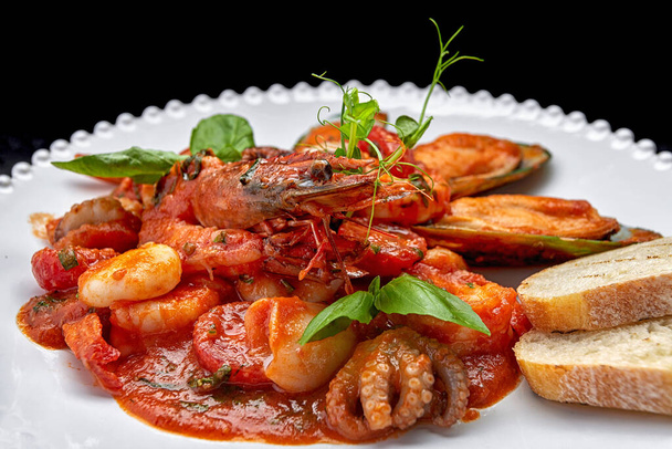 Sauteed seafood with shrimps, mussels, squid and scallop on a white plate, on a dark background - Photo, Image