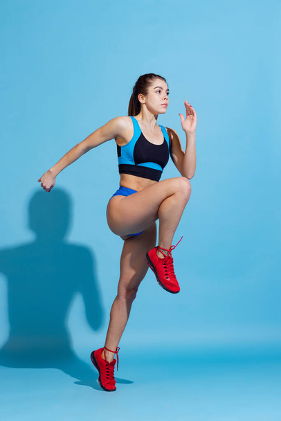 Young beautiful sportive girl training with sports equipment isolated on blue studio background. Sport, action, fitness, youth concept. - Foto, Imagem