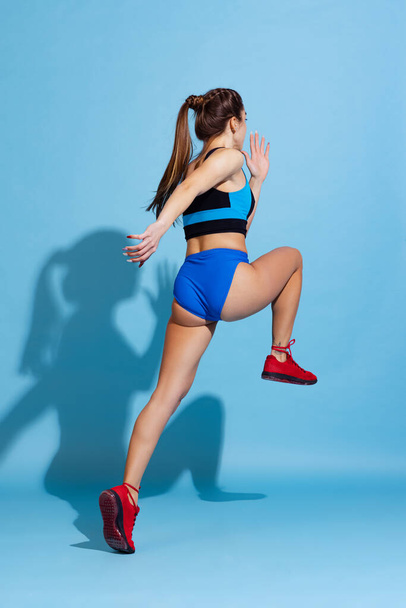 Young beautiful sportive girl training with sports equipment isolated on blue studio background. Sport, action, fitness, youth concept. - Fotografie, Obrázek