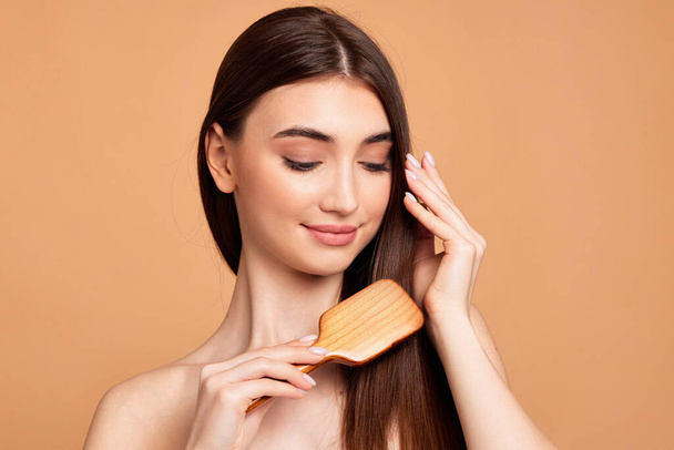 Beautiful woman combs her hair with wooden brush - Foto, Imagem
