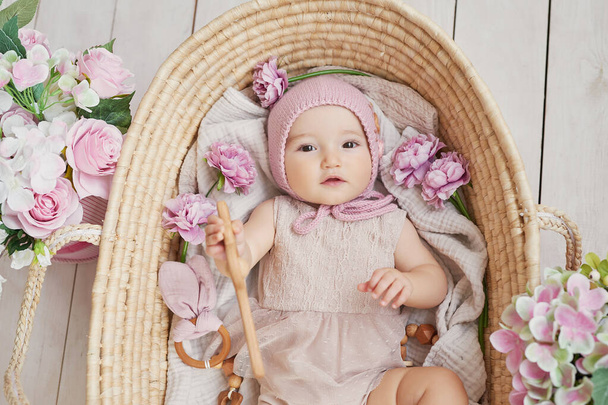 木製のラトルとウィッカーバスケットの花の帽子の赤ちゃんの女の子。ポストカード母の日とイースター。子供保護の日。世界幸福の日。笑顔の子供 - 写真・画像
