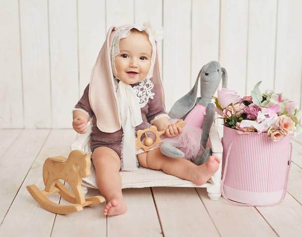 Маленькая девочка в шляпе с ушами в плетеной корзине с деревянными игрушками. День матери и Пасха. День защиты детей. Всемирный день счастья. Улыбающийся ребенок - Фото, изображение
