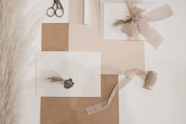 Top view of composition of sheets of paper, scissors, white envelope with grey wax seal, bow of transparent ribbon. - Фото, зображення