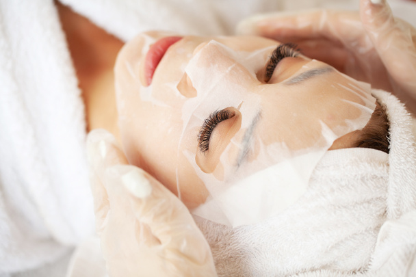 Schöne junge Frau verwendet Blatt Gesichtsmaske auf der Gesichtshaut für Beauty-Spa - Foto, Bild