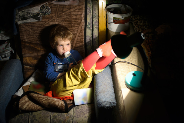 Enfant assis sur une chaise dans une pièce sombre devant la lampe
 - Photo, image