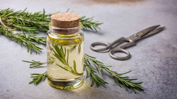 Tarro de vidrio de aceite de oliva con hierbas de cocina romero verde para una alimentación saludable sobre fondo de hormigón gris - Foto, imagen